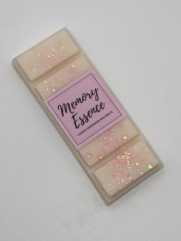A wax melt bar with a label reading 'MEMORY ESSENCE', covered in glitter and with a pink band at the top.